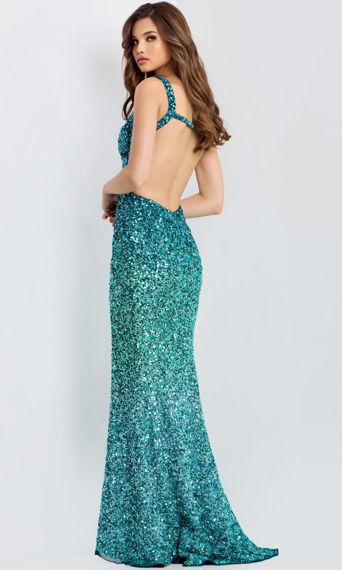 A woman models the Long Prom Dress: Jovani 46066—a sequin-embellished teal gown with an open back—as she stands against a plain light background, looking over her shoulder.